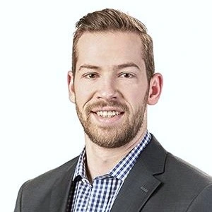 Cropped head shot of a smiling man with a
                                    short beard wearing a gray blazer over a
                                    checkered shirt.