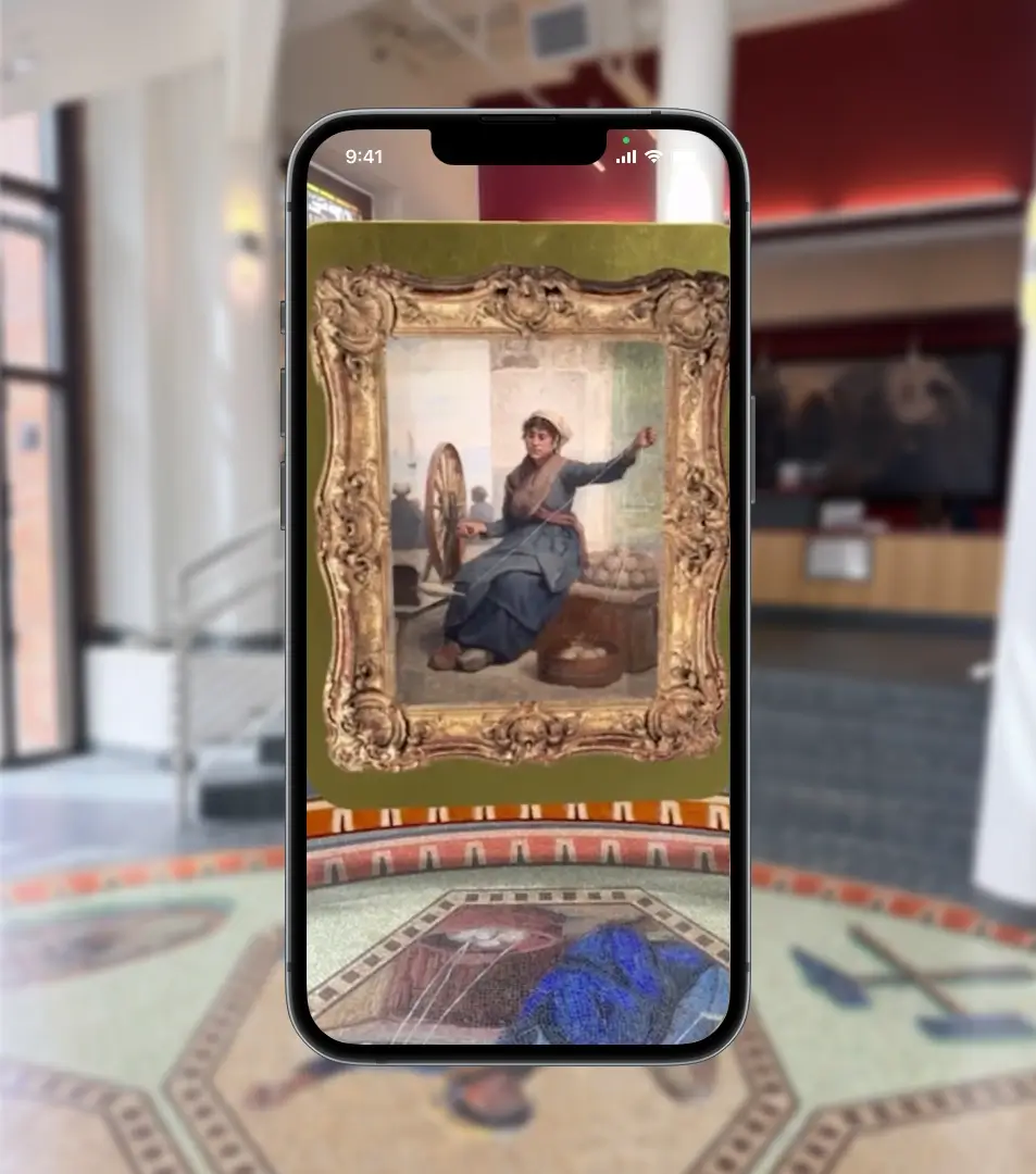 Smartphone displaying an augmented reality view
                                of a framed painting overlaid in a museum interior,
                                showing a seated woman spinning yarn within an
                                ornate gold frame.